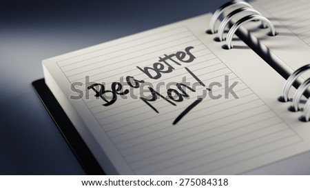 Closeup of a personal agenda setting an important date representing a time schedule. The words Be a better man written on a white notebook to remind you an important appointment.