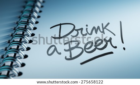 Closeup of a personal calendar setting an important date representing a time schedule. The words Drink a beer written on a white notebook to remind you an important appointment.