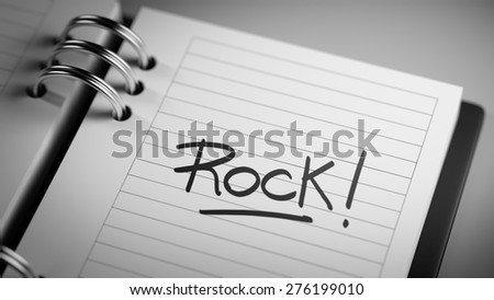 Closeup of a personal agenda setting an important date representing a time schedule. The words Rock written on a white notebook to remind you an important appointment.