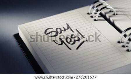 Closeup of a personal agenda setting an important date representing a time schedule. The words Say Yes written on a white notebook to remind you an important appointment.