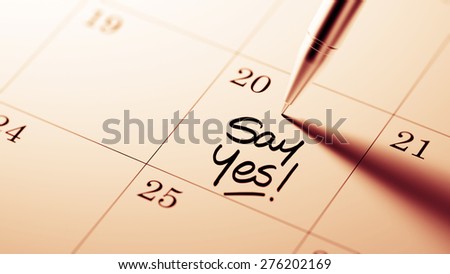 Closeup of a personal agenda setting an important date written with pen. The words Say Yes written on a white notebook to remind you an important appointment.