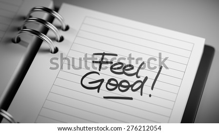 Closeup of a personal agenda setting an important date representing a time schedule. The words Feel Good written on a white notebook to remind you an important appointment.