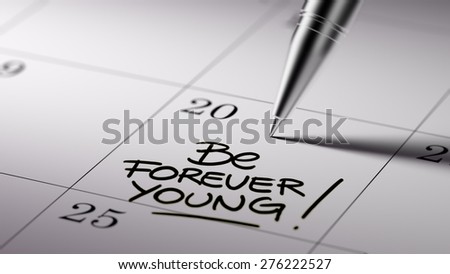Closeup of a personal agenda setting an important date written with pen. The words Be Forever young written on a white notebook to remind you an important appointment.