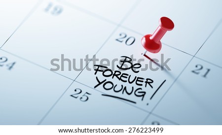 Concept image of a Calendar with a red push pin. Closeup shot of a thumbtack attached. The words Be Forever young written on a white notebook to remind you an important appointment.