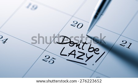Closeup of a personal agenda setting an important date written with pen. The words Don\'t be Lazy written on a white notebook to remind you an important appointment.