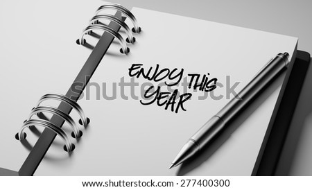 Closeup of a personal agenda setting an important date writing with pen. The words Enjoy this year written on a white notebook to remind you an important appointment.