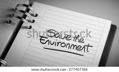 Closeup of a personal agenda setting an important date representing a time schedule. The words Save the environment written on a white notebook to remind you an important appointment.