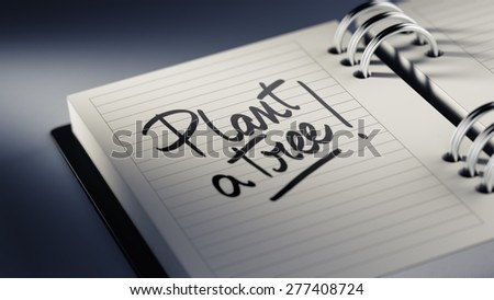 Closeup of a personal agenda setting an important date representing a time schedule. The words Plant a tree written on a white notebook to remind you an important appointment.