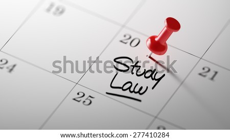 Concept image of a Calendar with a red push pin. Closeup shot of a thumbtack attached. The words Study Law written on a white notebook to remind you an important appointment.