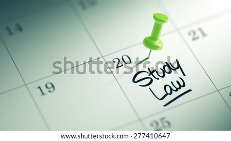Concept image of a Calendar with a green push pin. Closeup shot of a thumbtack attached. The words Study Law written on a white notebook to remind you an important appointment.