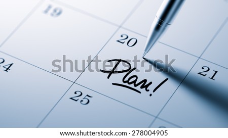 Closeup of a personal agenda setting an important date written with pen. The words Plan written on a white notebook to remind you an important appointment.