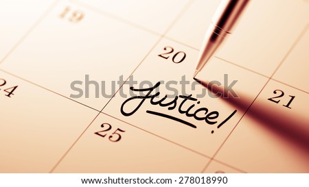 Closeup of a personal agenda setting an important date written with pen. The words Justice written on a white notebook to remind you an important appointment.