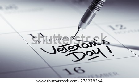 Concept image of a Calendar with a golden dart stick. The words Veteran\'s Day written on a white notebook to remind you an important appointment.