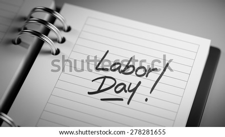 Closeup of a personal agenda setting an important date representing a time schedule. The words Labor Day written on a white notebook to remind you an important appointment.