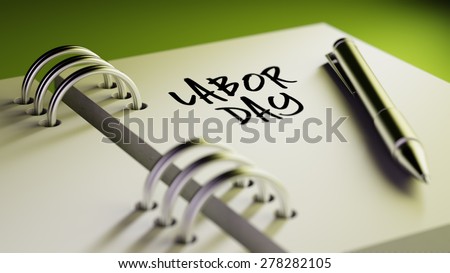 Closeup of a personal agenda setting an important date writing with pen. The words Labor Day written on a white notebook to remind you an important appointment.