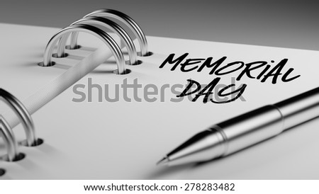Closeup of a personal agenda setting an important date writing with pen. The words Memorial Day written on a white notebook to remind you an important appointment.