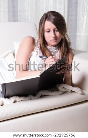 Pretty young girl on couch writing in Book