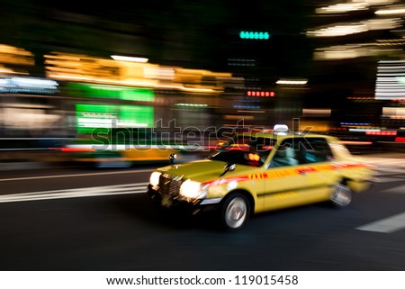 Yellow Tokyo taxi rushing through Tokyo downtown district at night.