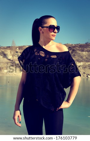 On a photo of a beautiful girl with black hair and sunglasses. She is wearing black blouse and black jeans.