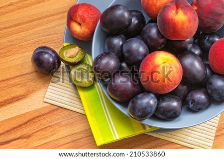 Delicious fresh plums and peaches in blue bowl on wood background.