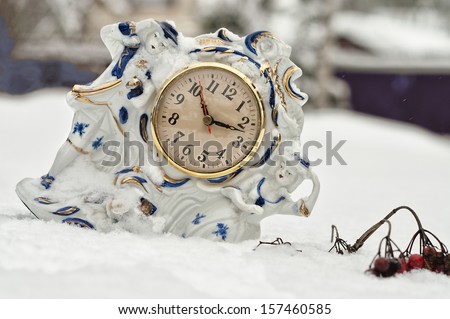 a porcelain mantel clock on the snow, concept of time passing or season change
