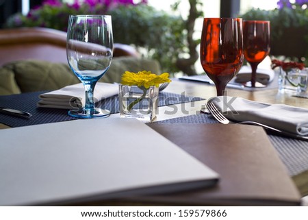 menu books in  cafe with wineglasses and a small yellow flower in the middle of composition
