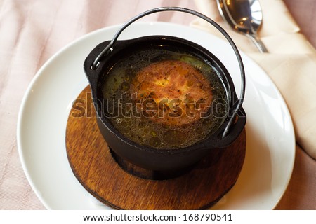 hot soup with beef and tomato in cast iron traditional pot, standing on the wooden tray on the laid table, overhead shot