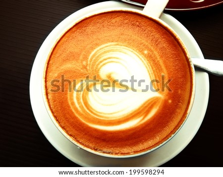 heart shape foamed latte in a white cup and saucer, overhead shot