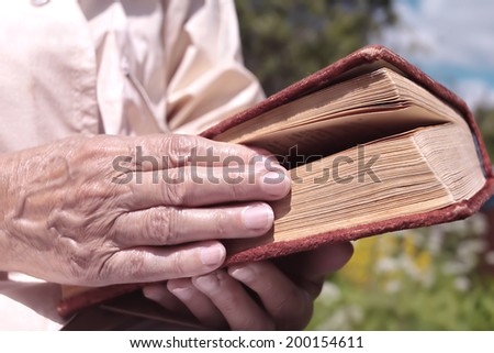 Female hand holding an old book, concept of reading and knowledge. Outdoor shot with particular focus on the hand and book.