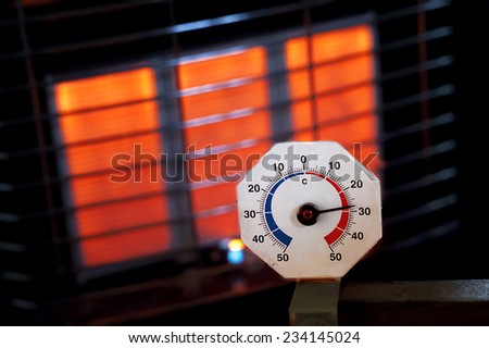 It is getting warmer, close up of an old analogue thermometer with a gas heater in the background