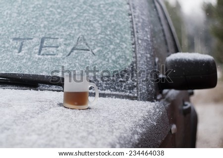 Cup of hot tea on a snowy car hood, concept of engine start in cold weather