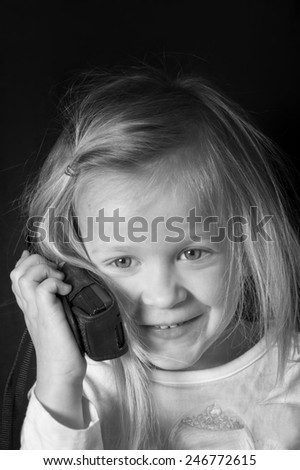 Little cute girl with messy hair on a retro mobile phone, studio vertical shot in black and white