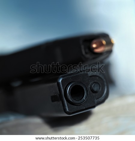 Close up of a hand gun barrel with a muzzle and loaded magazine in the blurred background
