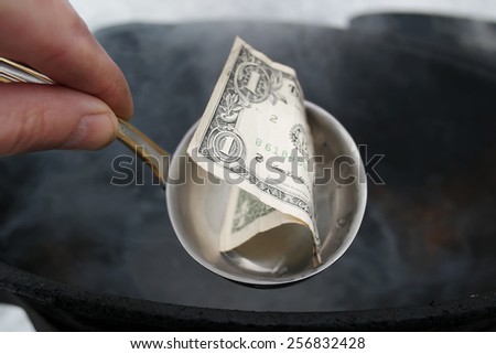 Male hand holding ladle with a dollar bill instead of food, boiling pan in the background, concept of impoverishment