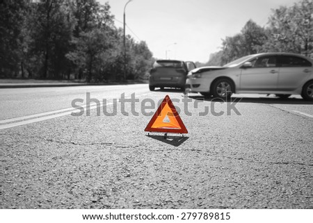 Hazard warning triangle laid out on the road  behind two crashed cars, black and white photo with a  red accent on a triangle