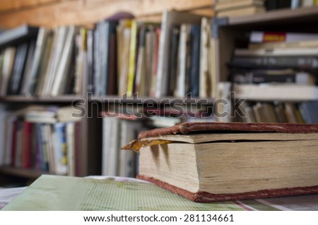 Closeup of an old book in the foreground and bookshelves in the blurred background, indoor horizontal shot with shallow depth of field
