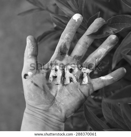 Painted word Art on a human hand, green foliage in the blurred background, concept of visual arts