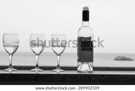 Bottle of abstract alcohol drink and glasses on a window, sea in the blurred background.