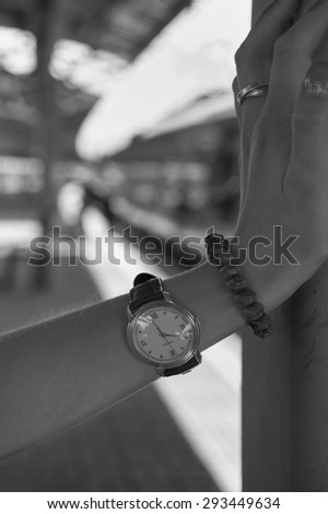 Wrist Watch on a female hand in focus, railway station and train in the blurred background