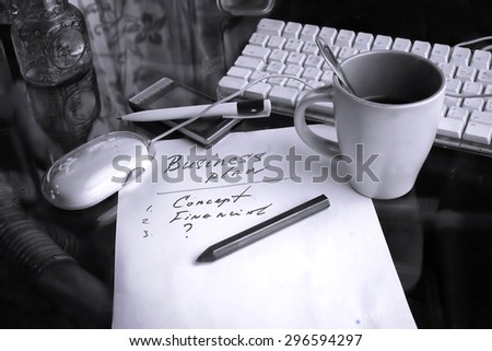 Hand written text Business Plan, computer keyboard, mug of tea and mobile phone around. Still life in black and white