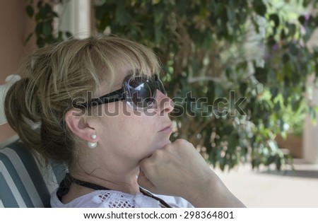 Mid aged woman wearing sun glasses relaxing or waiting in a park, outdoor horizontal shot