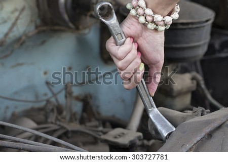 Closeup of a female hand holding wrench next to car radiator, concept of cars repair