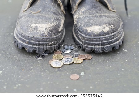 Coins next to beggar wearing old shoes, front shot with particular focus