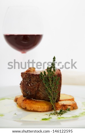 roast meat with potatoes on white plate with glass of wine