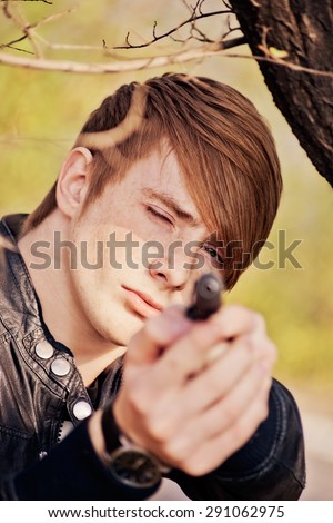 attractive, aggressive red-haired guy with a gun in nature. close-up portrait