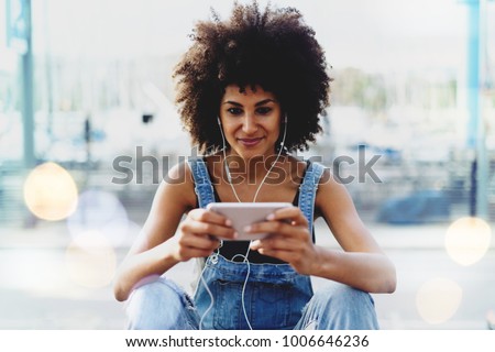 charming dark-skinned girl with afro hair watching video on mobile phone using public network wifi outside. Modern female entrepreneur communicates via video link with her personal assistant