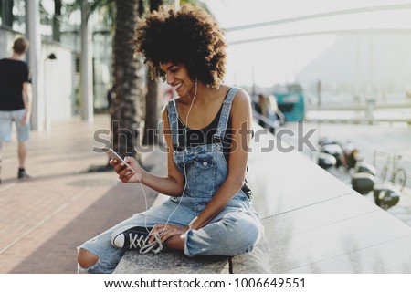 beautiful mixed race girl with afro hair listening to her favorite music through headphones using a mobile phone. an attractive black young woman adds a new track to her playlist using a mobile app