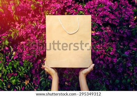 woman holding a bag on a background of flowers. flare light. girl holding a paper bag with both hands