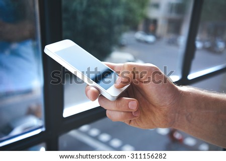 Man using mobile smart-phone near the window, closeup