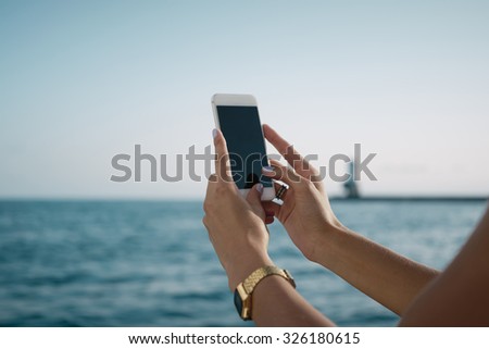 Young female shooting seascape on her smart-phone on a sea background